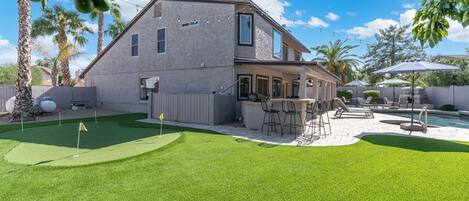 Una casa con un patio trasero que incluye piscina, mobiliario exterior y un campo de práctica de golf.