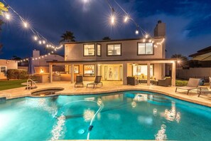 A modern two-story house with a swimming pool, outdoor seating, and string lights.