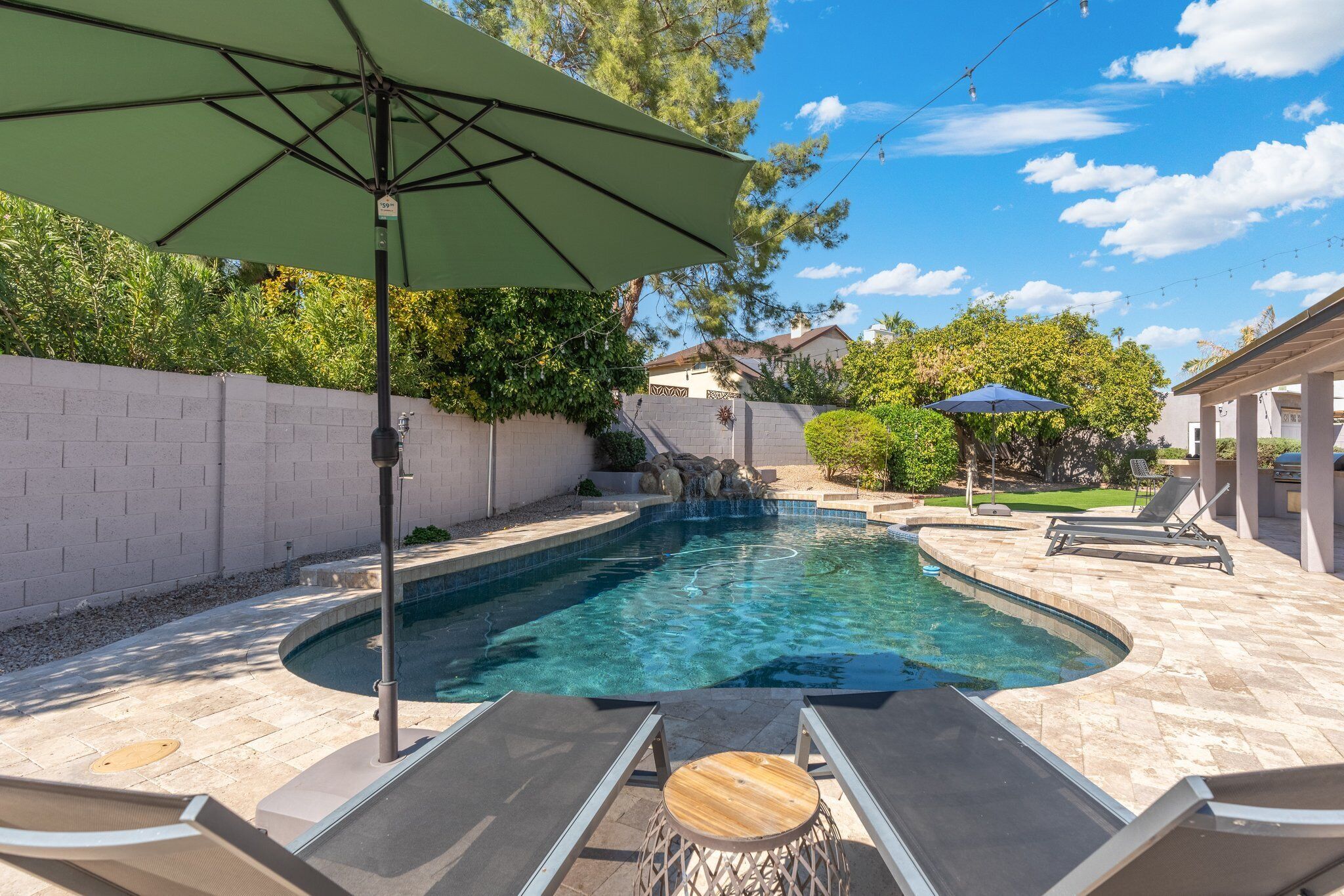 A swimming pool with a waterfall feature, surrounded by lounge chairs and a pergola.