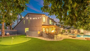 Uma casa com quintal que inclui piscina, um terraço com mobiliário de exterior e área bem iluminada com luzes de cordão.
