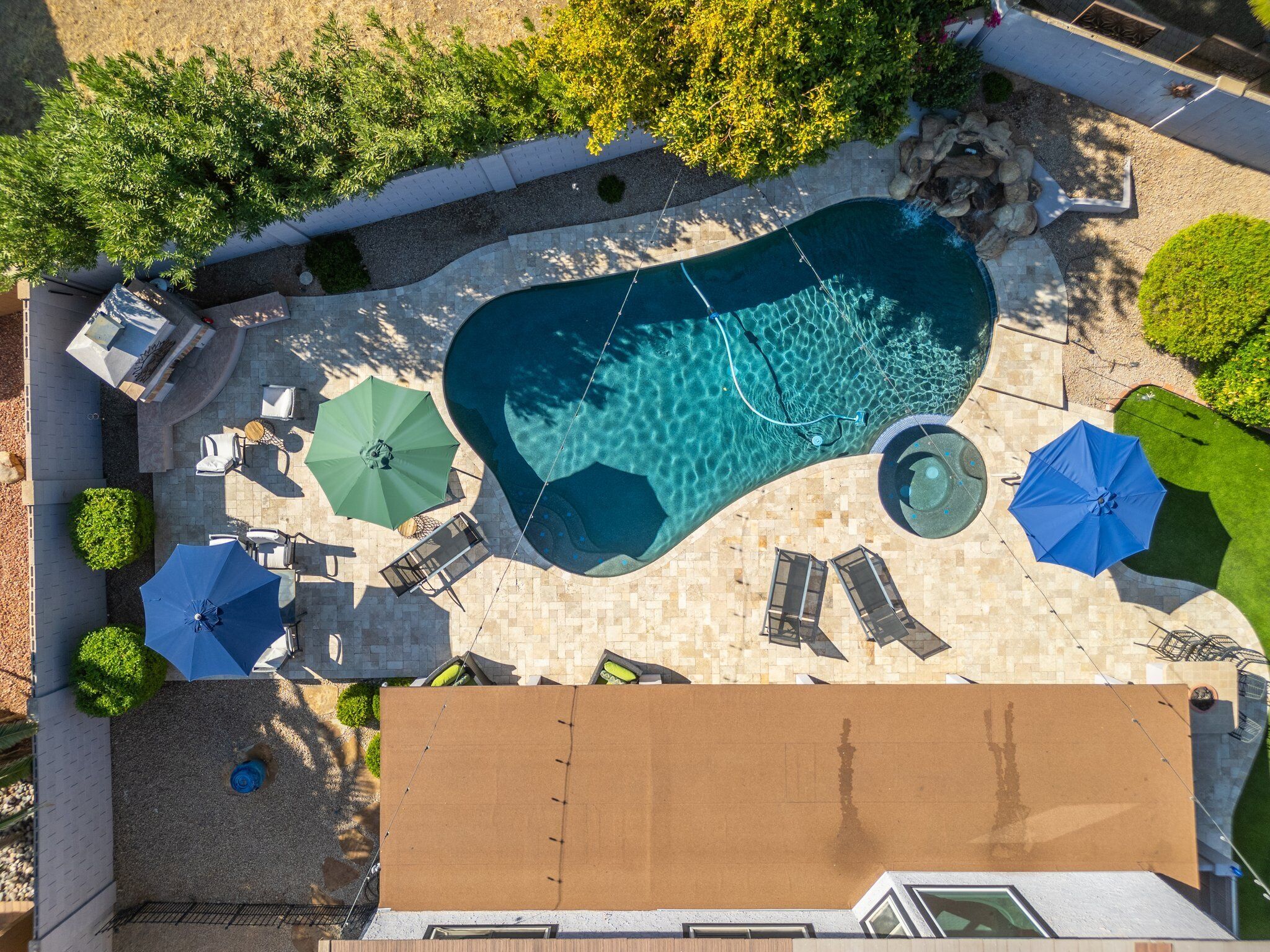 An aerial view of a swimming pool with lounge chairs and umbrellas, surrounded by greenery and stone pathways.