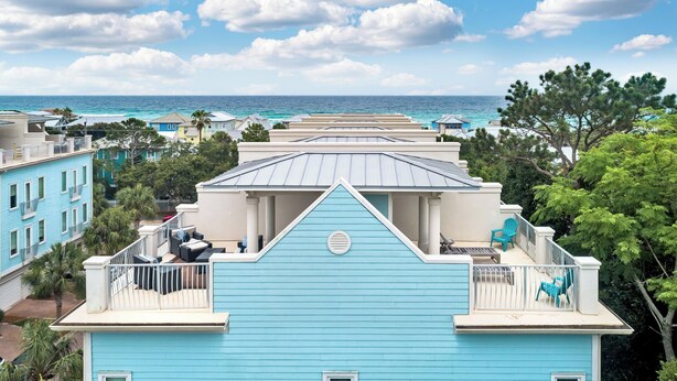 Et kystnære boligområde med et blåt hus, der har en balkon med udesiddeplads og udsigt til havet.