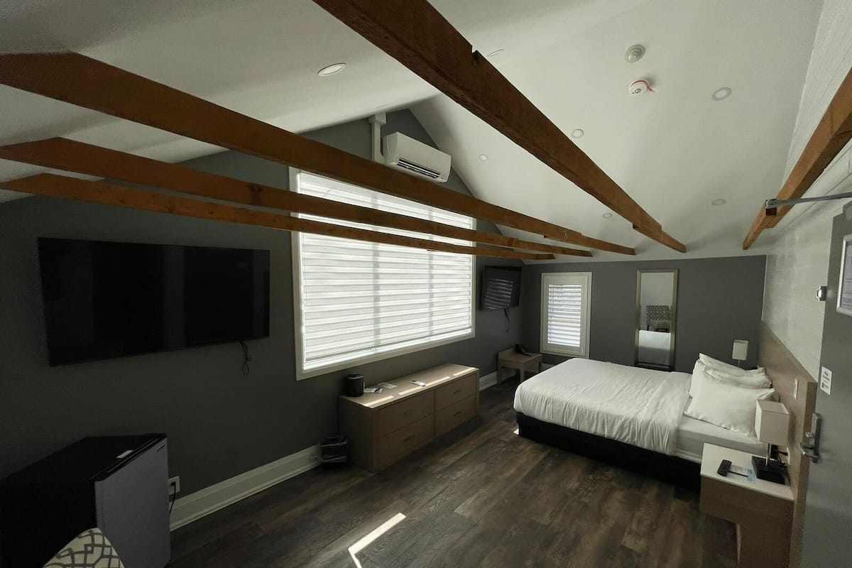 Un dormitorio con cama, mesitas de noche, televisor y ventana con persianas.