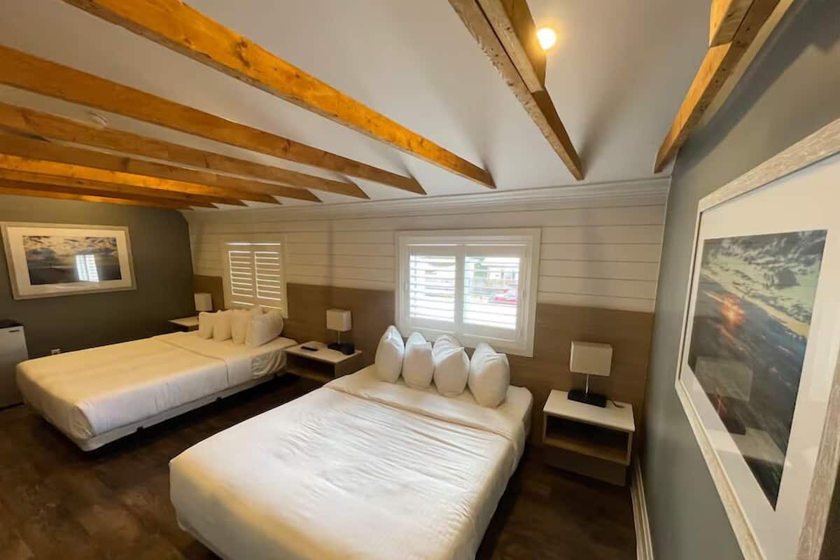 Habitación de hotel con dos camas, vigas de madera en el techo, un ventanal grande y un cuadro en la pared.