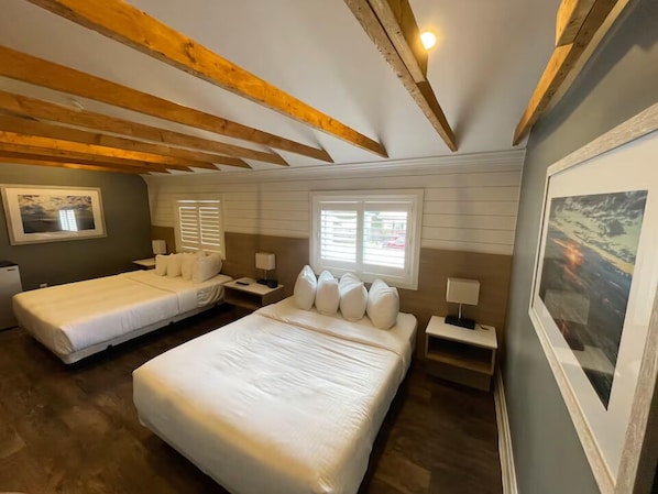 Habitación de hotel con dos camas, vigas de madera en el techo, un ventanal grande y un cuadro en la pared.