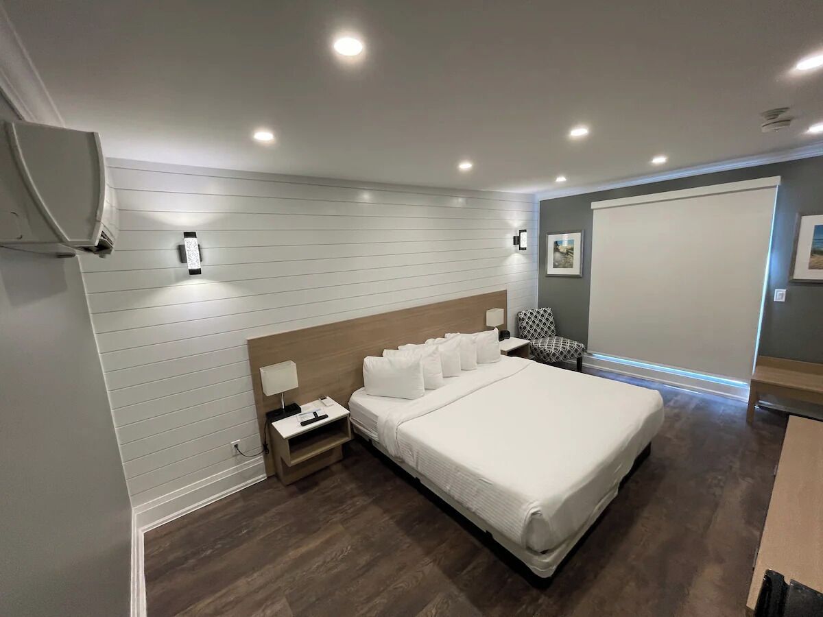 Una habitación de hotel moderna con una cama grande, mesitas de noche, un armario y un ventanal amplio.