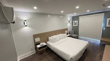 Una habitación de hotel moderna con una cama grande, mesitas de noche, un armario y un ventanal amplio.