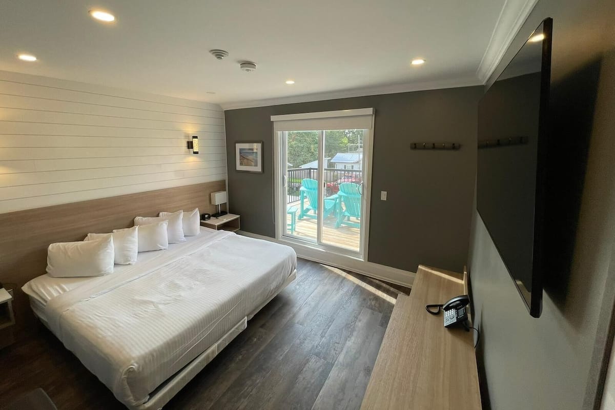 Habitación de hotel con cama, escritorio, silla, televisor y puerta corrediza de vidrio que da a un espacio exterior.
