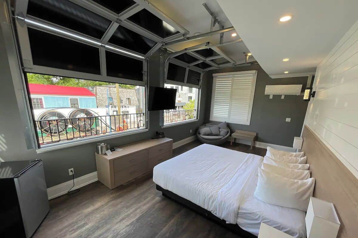 Un dormitorio moderno con una cama grande, un banco empotrado, un escritorio pequeño y una ventana con vistas al exterior.