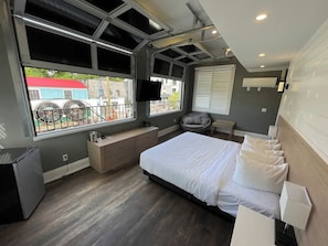 Un dormitorio moderno con una cama grande, un banco empotrado, un escritorio pequeño y una ventana con vistas al exterior.