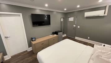 A modern bedroom with a bed, a bedside table with a phone, a flat-screen TV mounted on the wall, and an air conditioning unit.