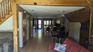 A spacious living area with a red sofa, a wooden staircase, and a kitchen in the background. - A-frame home on Trout Stream (Stoddard)