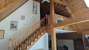 A wooden interior with a staircase, ceiling fan, and wall decorations including fish and tree silhouettes. - A-frame home on Trout Stream (Stoddard)