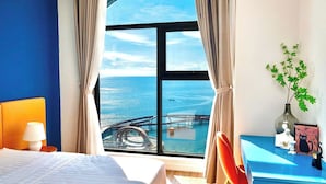 Een hotelkamer met een groot raam met uitzicht op zee en een brug. Er is een bed, een bureau en een stoel.