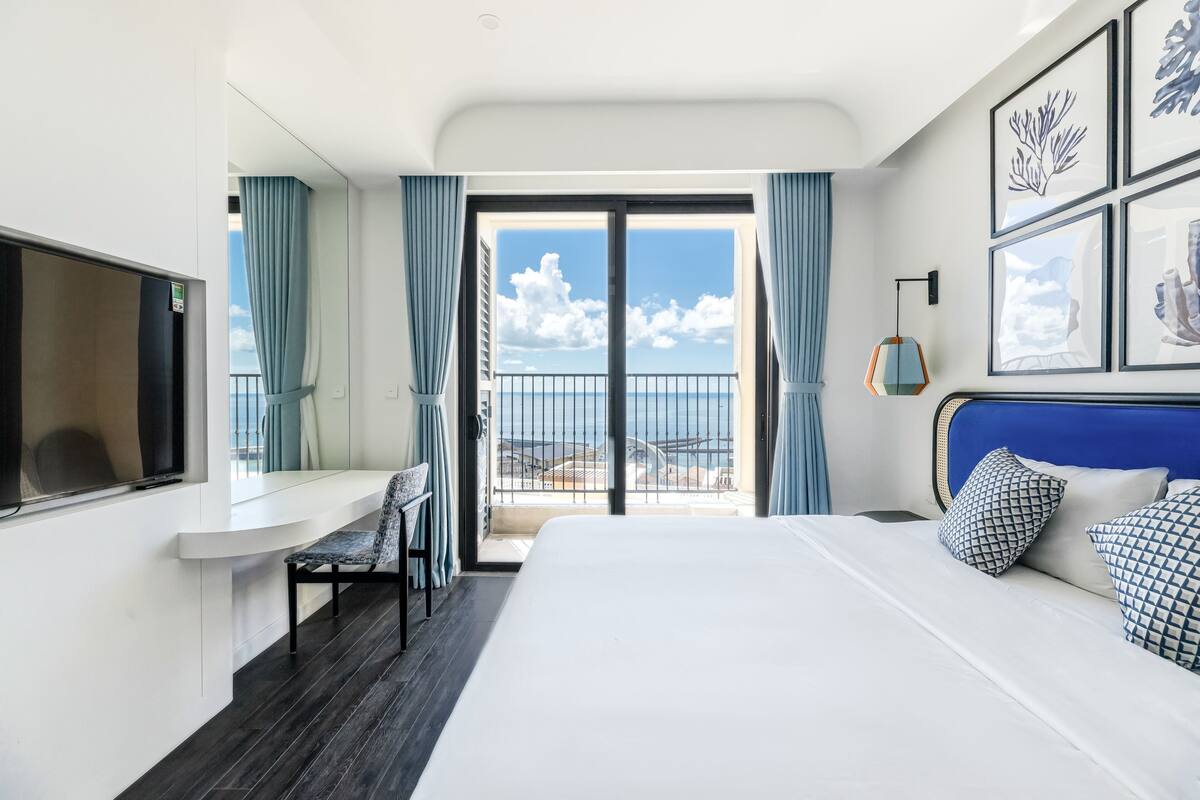 Une chambre d’hôtel comprenant un lit, un bureau, une chaise, une télévision et un balcon avec vue sur la mer.