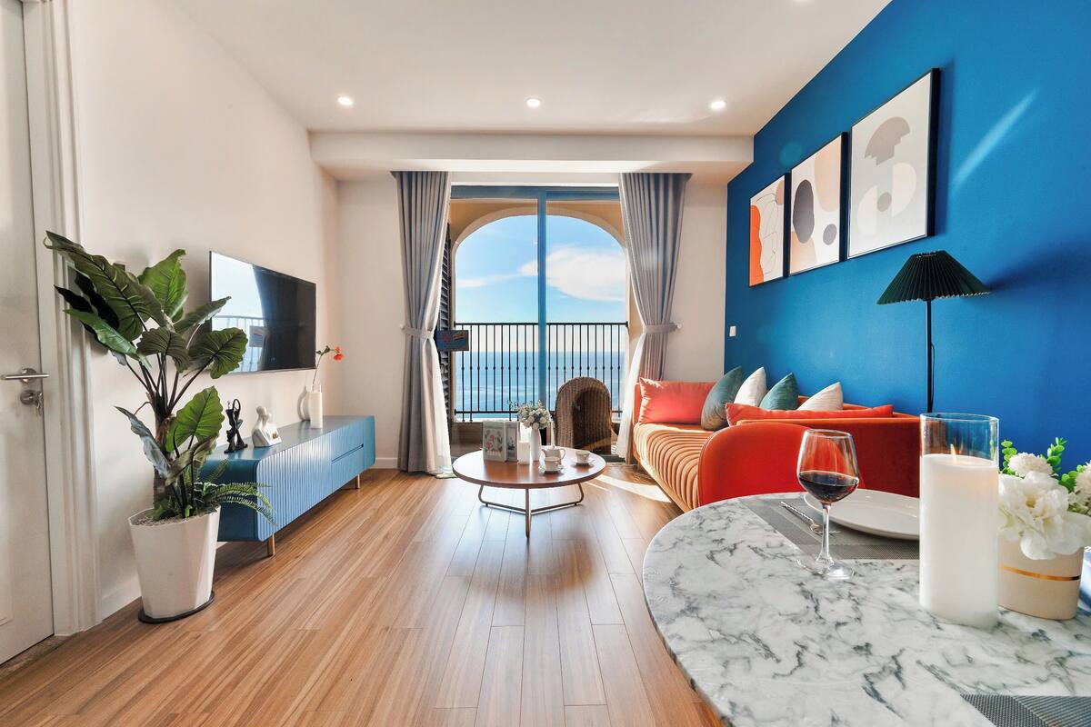 Un salon moderne avec un balcon, un téléviseur à écran plat, une table basse ronde et un canapé avec des coussins.