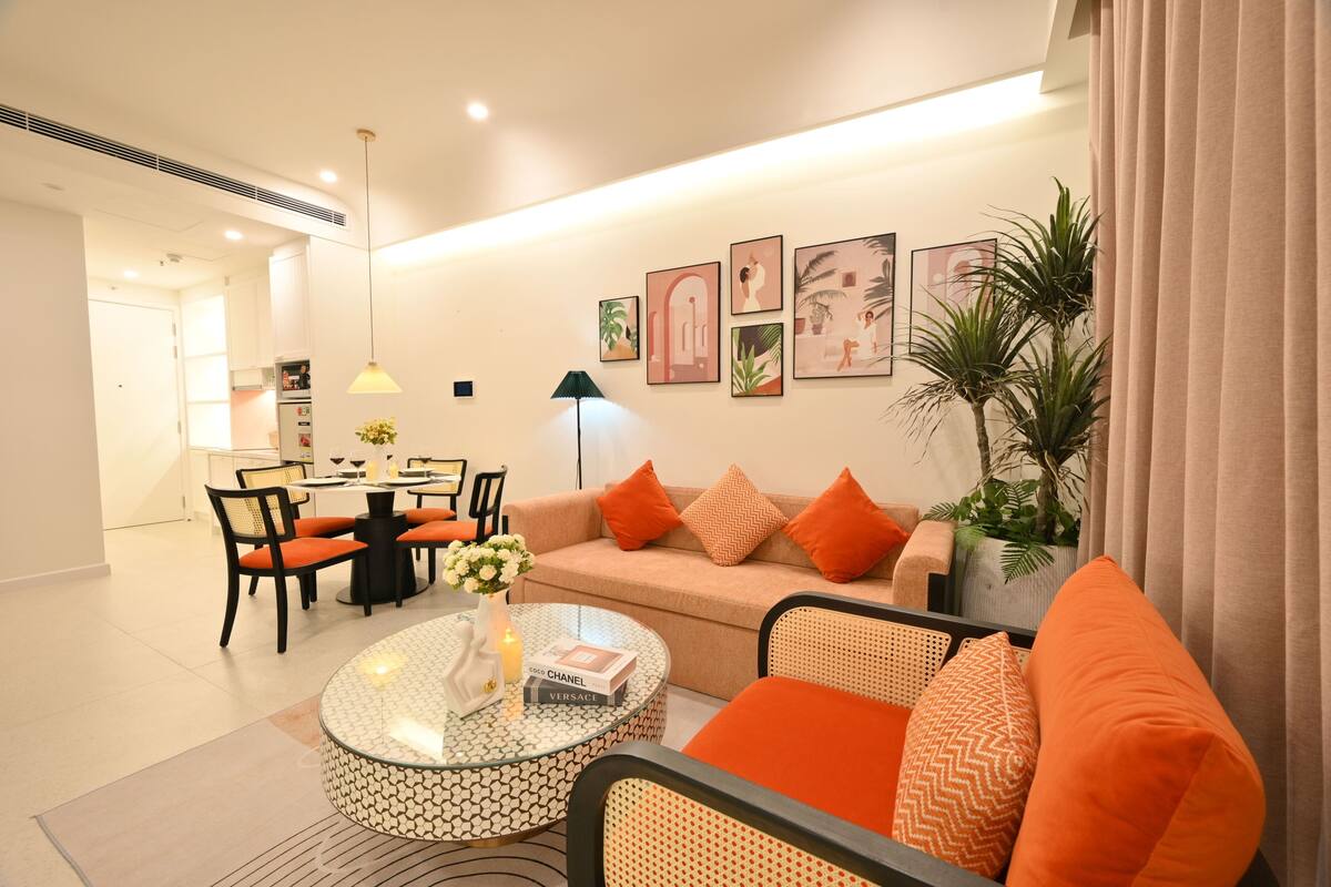 Un salon moderne comprenant un canapé, des fauteuils, une table à manger et une table basse. Des tableaux encadrés ornent le mur, et une plante en pot y est également présente.