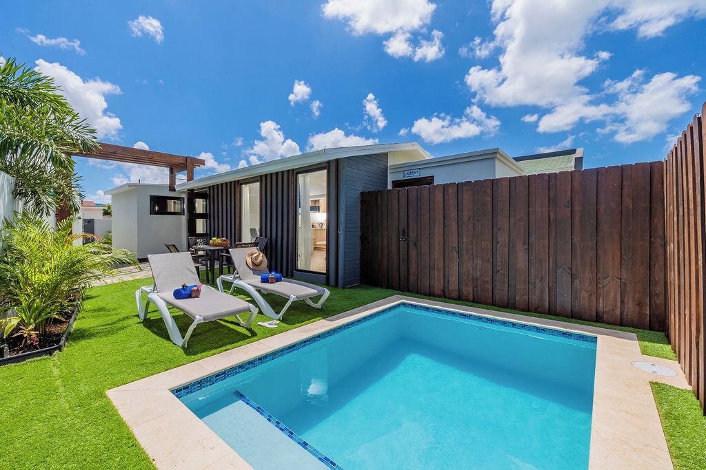 Un jardin avec une piscine, deux chaises longues, une clôture en bois et un petit espace patio comprenant une table et des chaises.
