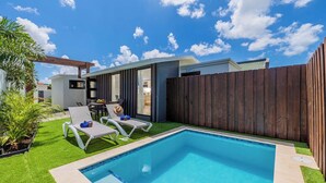 A backyard with a swimming pool, two lounge chairs, a wooden fence, and a small patio area with a table and chairs.