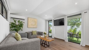 A modern living room with a grey sofa, a wooden coffee table, and a large window with a view of the outdoors.