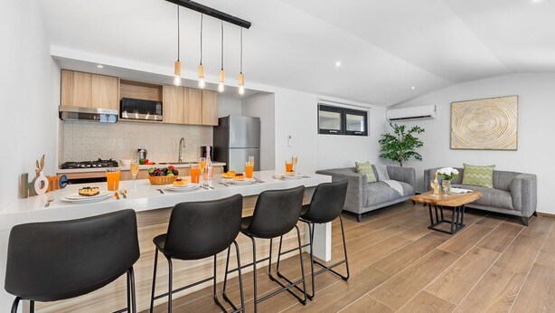 A modern kitchen with a central island, bar stools, and a dining area.
