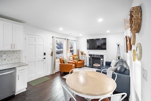 A modern living room with a fireplace, a TV, and a dining area. - Buttercup Hideaway; Cozy oasis near WFU, Reynolda Gardens & Historic Graylyn (Winston-Salem)