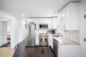A modern kitchen with white cabinetry, stainless steel appliances, and a patterned backsplash. - Buttercup Hideaway; Cozy oasis near WFU, Reynolda Gardens & Historic Graylyn (Winston-Salem)