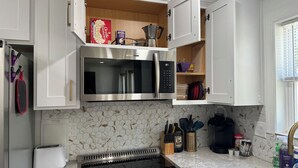 Una cocina moderna con armarios blancos, microondas integrado, estufa de acero inoxidable y un salpicadero de azulejos hexagonales.