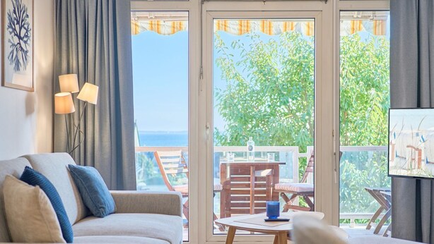 Un salon avec un canapé, une table et un téléviseur. Il y a un balcon avec une table et des chaises.