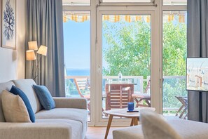 Ein Wohnzimmer mit Sofa, Tisch und Fernseher. Ein Balkon mit Tisch und Stühlen ist ebenfalls vorhanden.