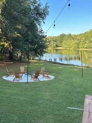 A backyard with a fire pit, wooden chairs, and a string of lights.