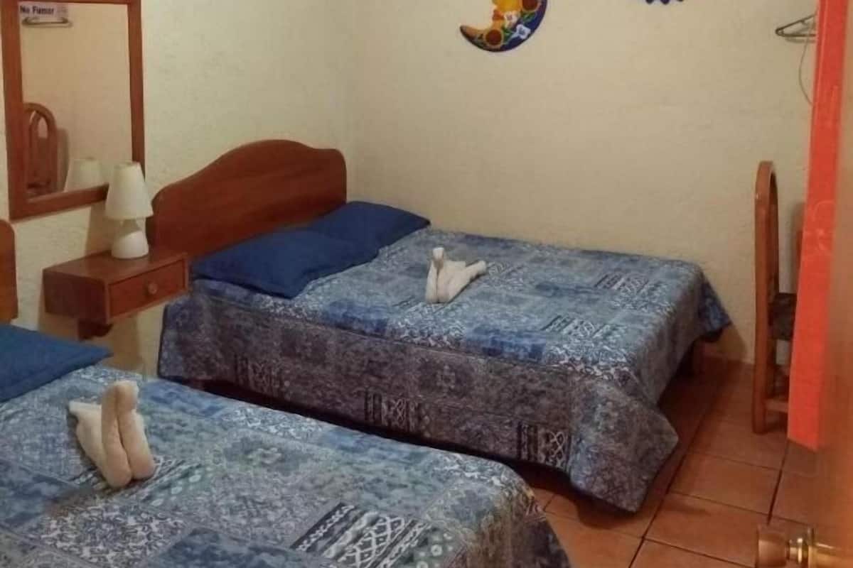 Una habitación con dos camas, un ventilador de techo, un reloj de pared y un espejo.