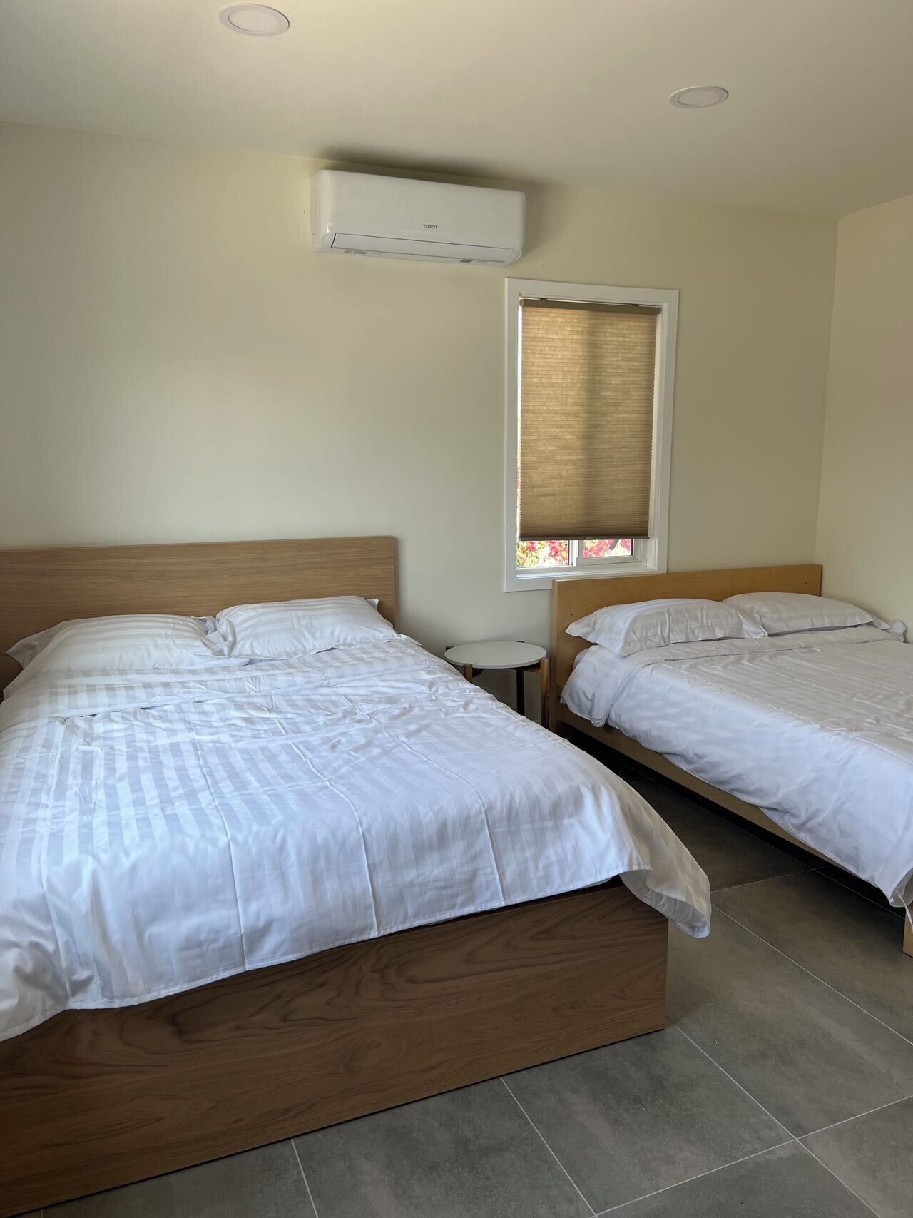 A hotel room with two beds, a window with a blind, and an air conditioning unit on the wall.