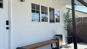 Un porche cubierto con un banco, un cubo de basura y una planta en maceta.