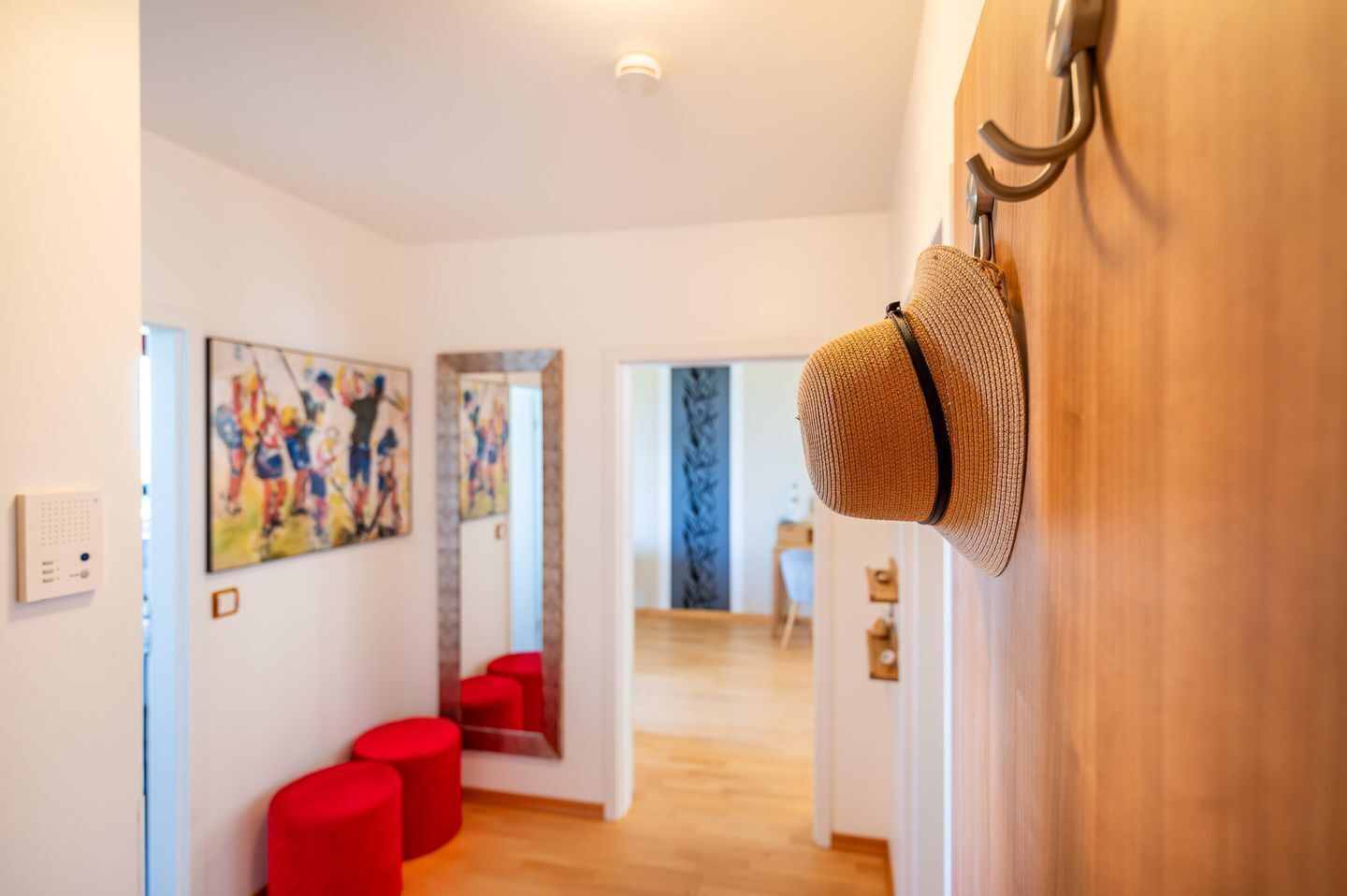 Ein Korridor mit Holzboden, einer roten Bank und einem Strohhut an der Wand.