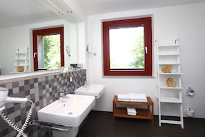 A modern bathroom with two sinks, a hairdryer, a towel rack, and a window with a red frame.