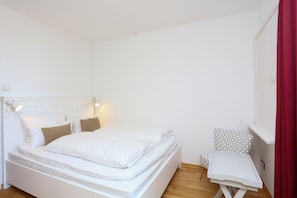 A minimalist bedroom with a bed, bedside table, and a small table with a patterned chair.