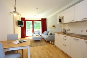 A modern living room with a sofa, a dining table with chairs, a kitchen area with cabinets and a microwave, and a television.
