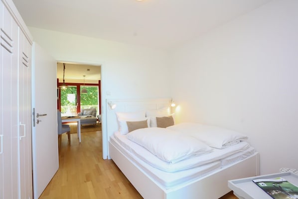 A bedroom with a bed, bedside table, and a view of the balcony.