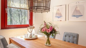 A dining area with a wooden table, chairs, a vase with flowers, a decorative lantern, and framed pictures on the wall.