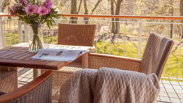 A balcony with wicker furniture, a table with a newspaper, and a vase with flowers.