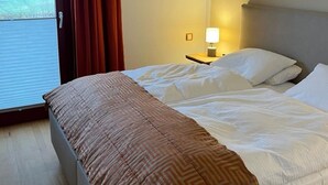 A hotel room with a bed, a nightstand, a lamp, and a view of a field through a window.