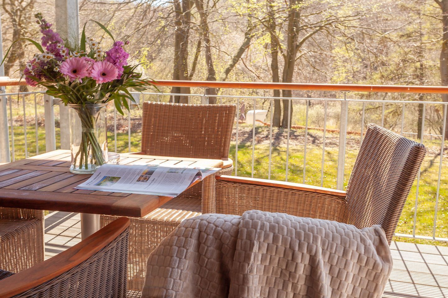 A wicker table and chairs on a balcony with a newspaper and a vase of flowers.