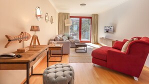 Una sala de estar moderna con un sofá rojo, un reposapiés gris, una mesa de centro de madera, otro sofá gris y un escritorio de madera con una lámpara.