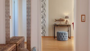 Una habitación con piso de madera, un otoman azul, una mesa de madera con una lámpara y una pared con un diseño ondulado.