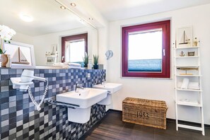 Une salle de bain moderne avec des carreaux à motifs, deux lavabos, un sèche-cheveux, un banc en bois et une fenêtre donnant sur un beau paysage.
