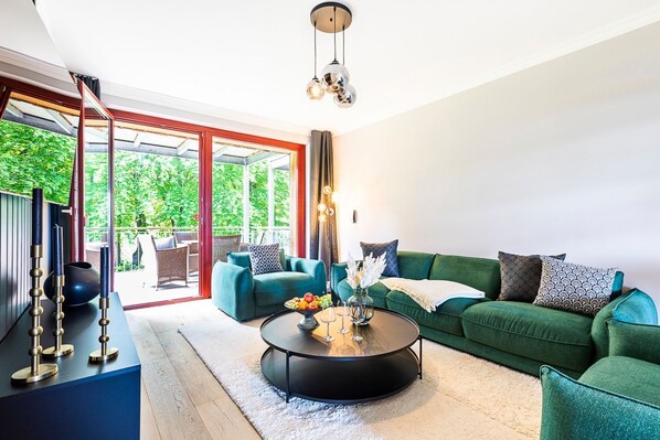 Un salon moderne avec un canapé vert, une table basse ronde et une table en verre sur laquelle sont disposés des fruits et des verres.