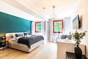Une chambre moderne avec un grand lit, un bureau et une vue sur la verdure par les fenêtres.