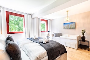 A modern bedroom with two beds, large windows with red frames, a tripod lamp, and a painting on the wall. - House Fore - Apartment Kreidefelsen - House Fore Apartment "Kreidefelsen" (Lohme)