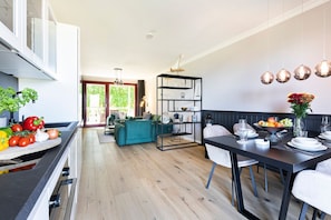 A modern kitchen with a dining area, a teal sofa, and a black dining table set for six. - House Fore - Apartment Kreidefelsen - House Fore Apartment "Kreidefelsen" (Lohme)